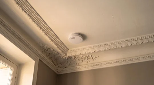 Détecteur de fumée installé au plafond moulure d'un appartement français, symbole de la sécurité incendie domestique